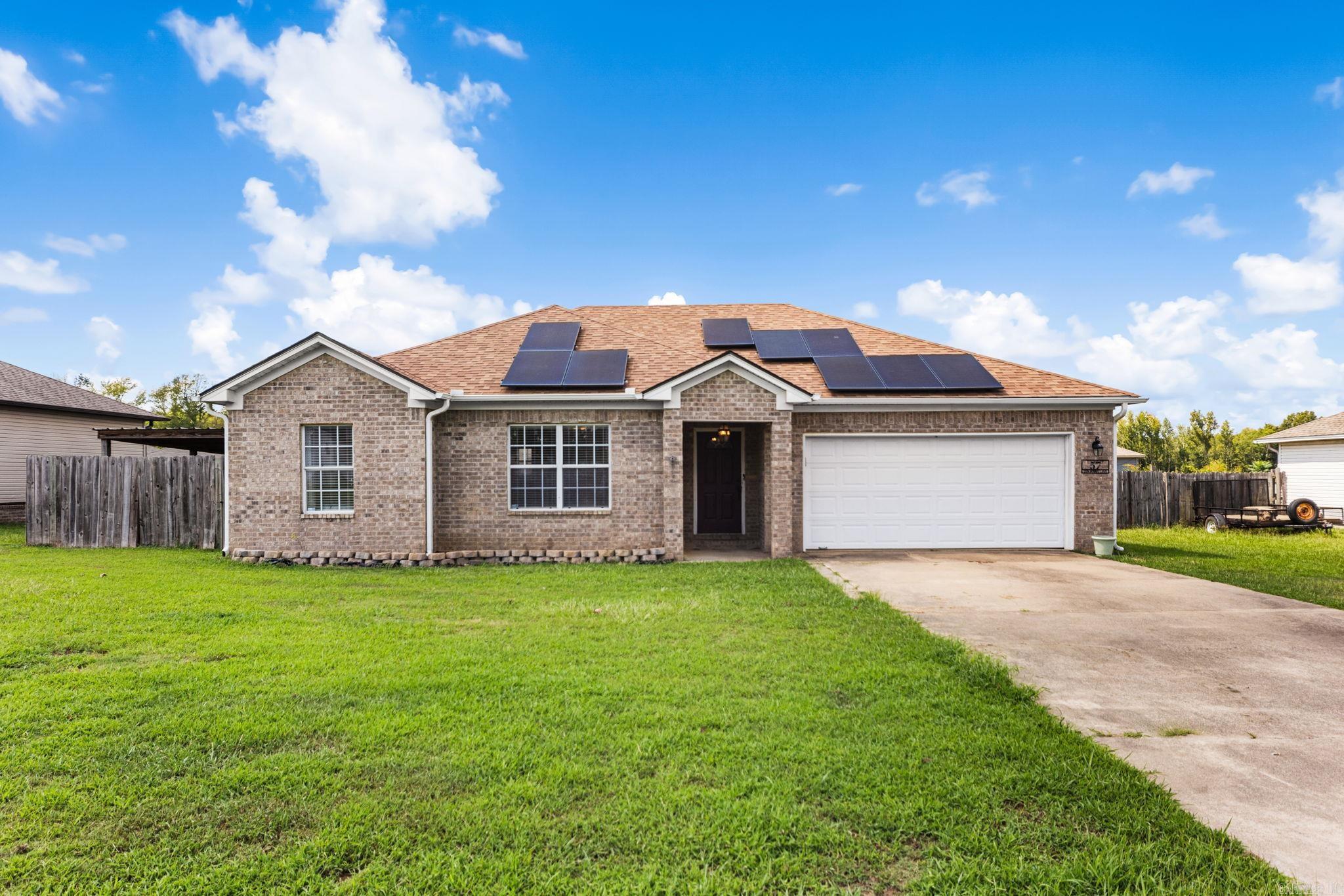 Single-story brick home with rooftop solar panels, a two-car garage, and a wide front lawn.