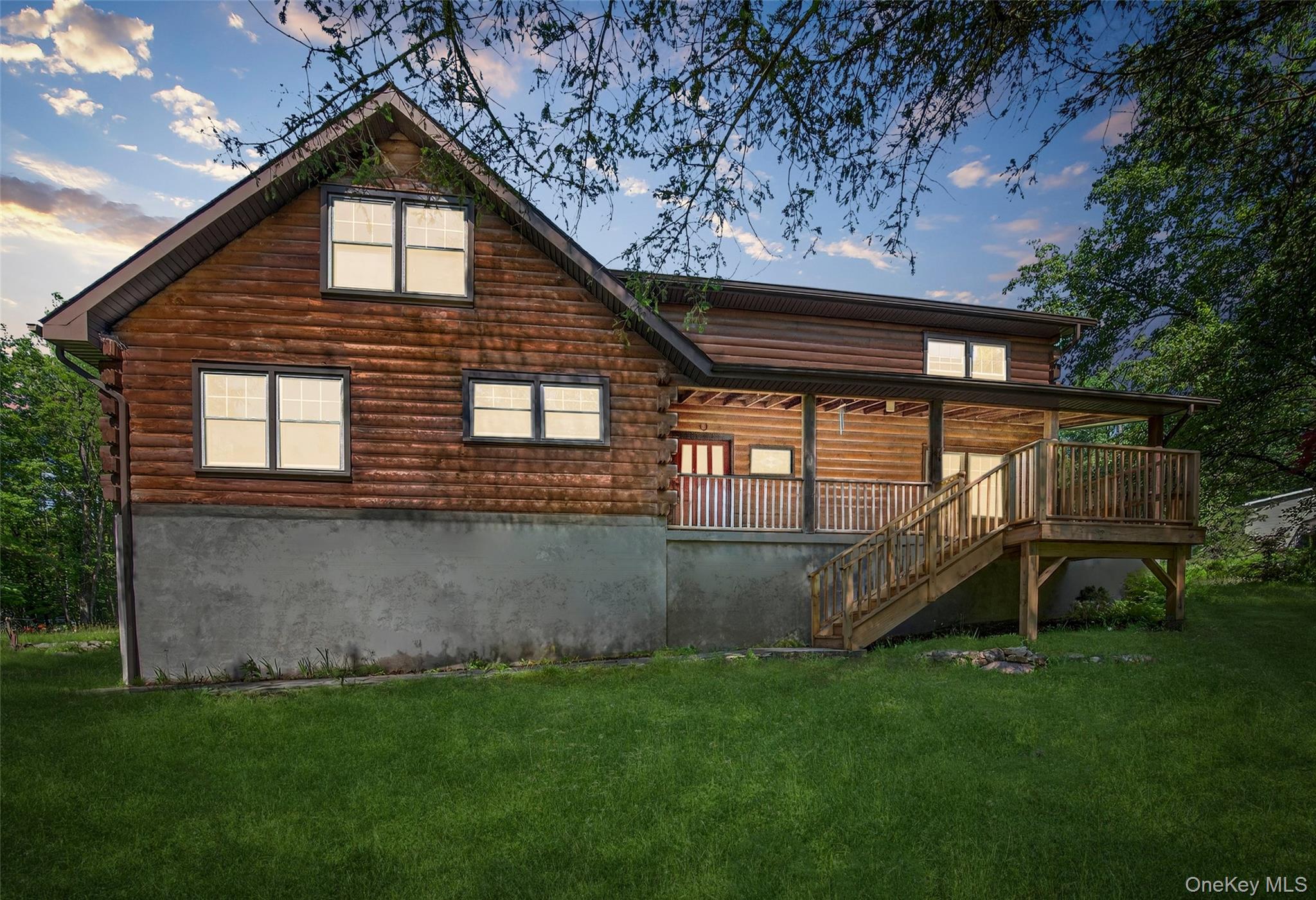 Log-sided home with a raised covered porch and wooden stairs overlooking a broad lawn.