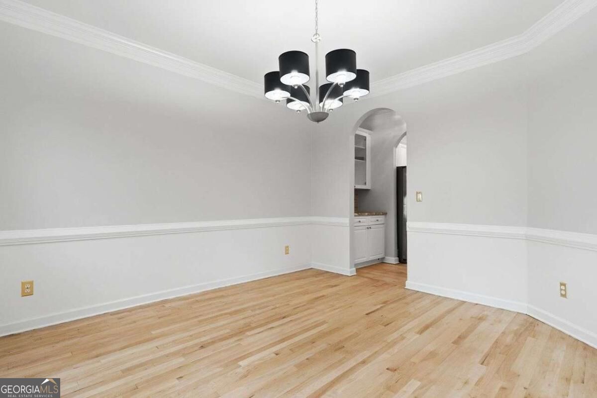 Empty dining room with hardwood floors, decorative molding, and a chandelier.