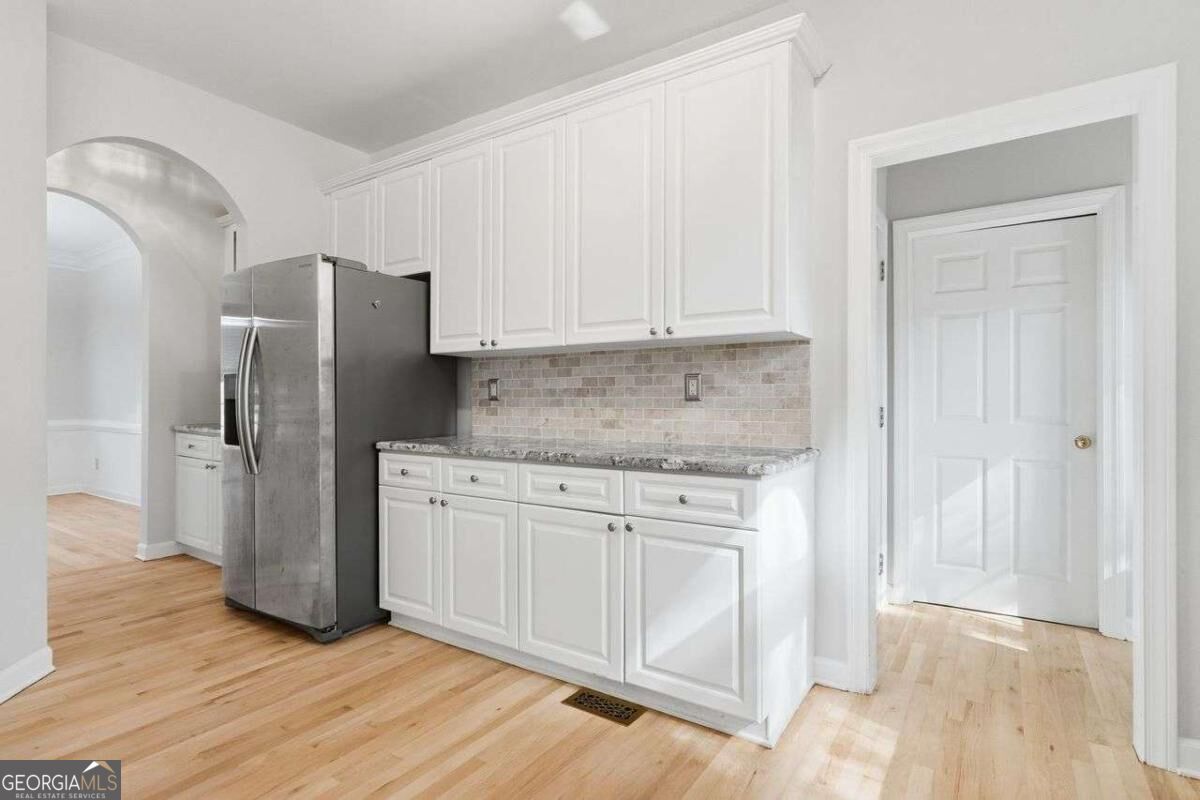 Kitchen with white cabinetry, stainless steel refrigerator, granite countertops, and light tile backsplash.