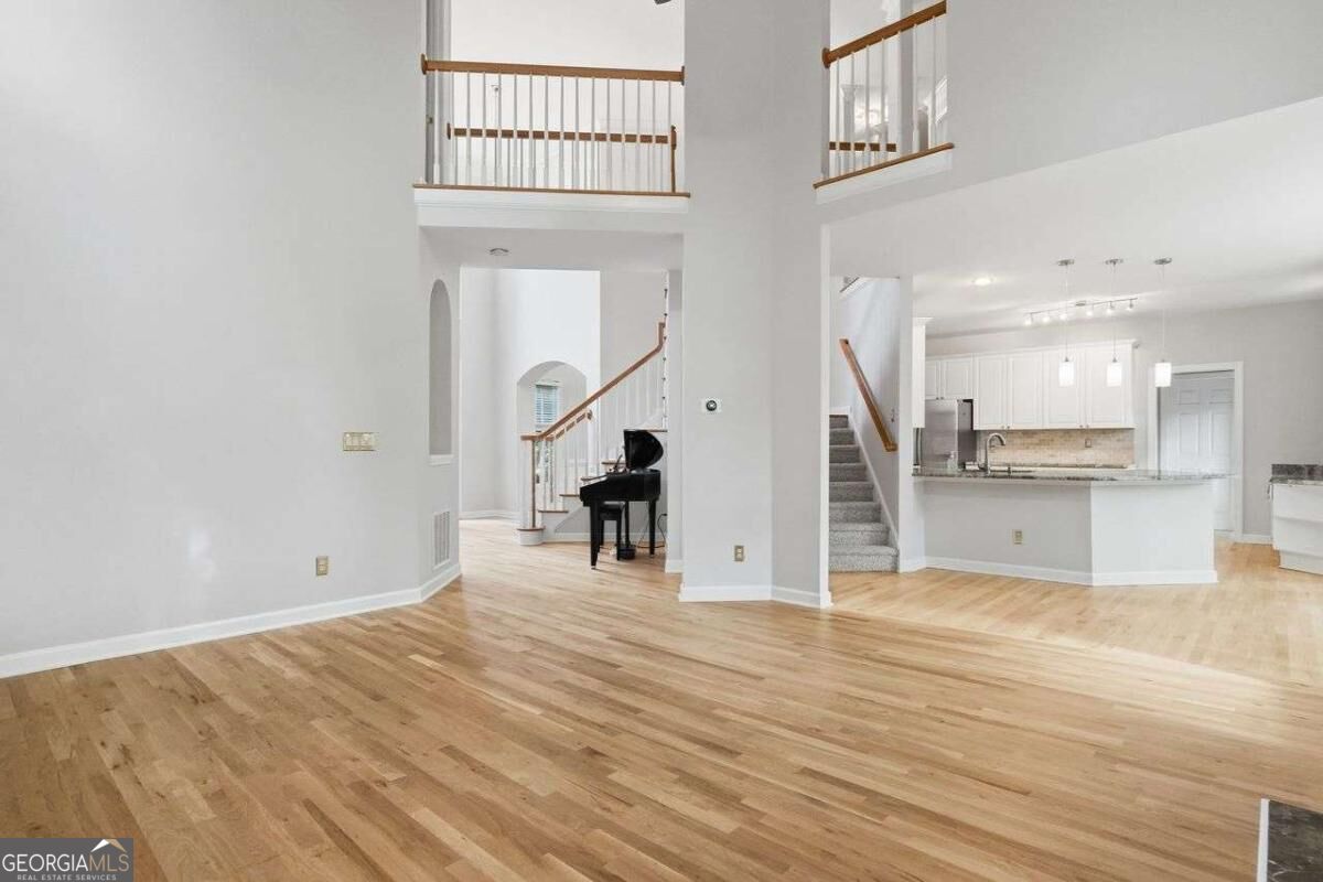 Open two-story living area with hardwood floors, an upstairs balcony, staircase, and white kitchen.