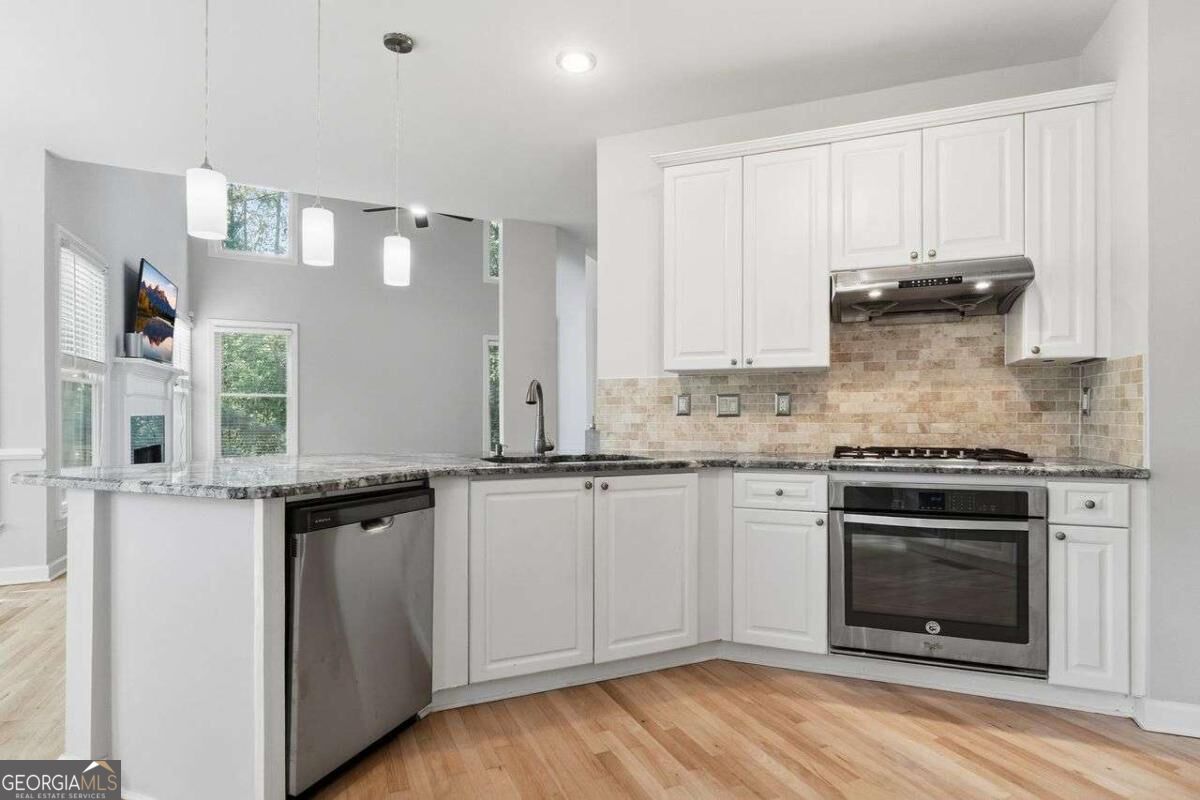 Kitchen with white cabinets, granite counters, tiled backsplash, stainless steel appliances, and a peninsula.