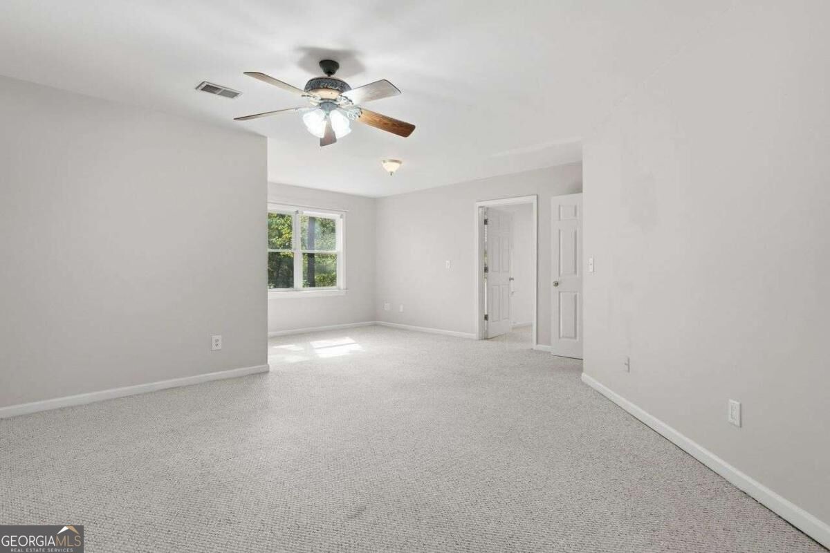 Empty carpeted bedroom with a ceiling fan, sunlit window, and two white doors.