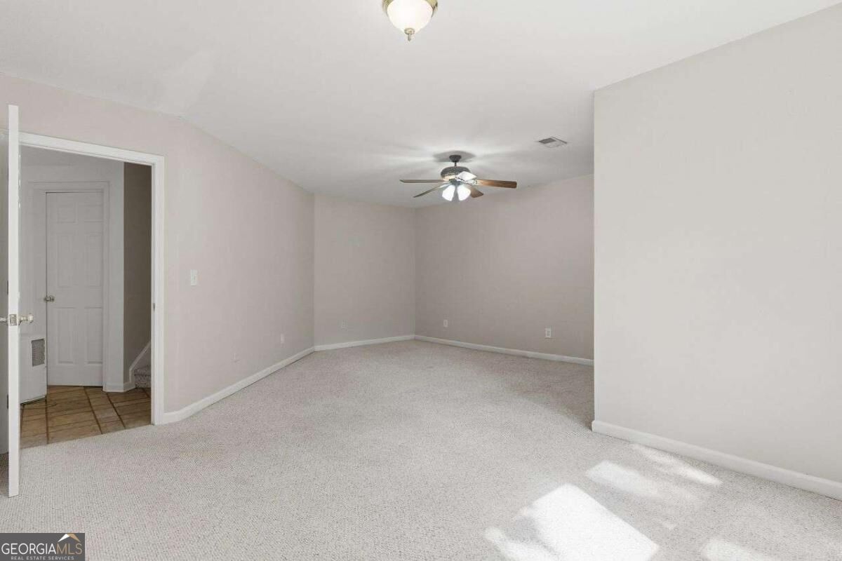 Empty carpeted room with a ceiling fan and doorway to a tiled hall.