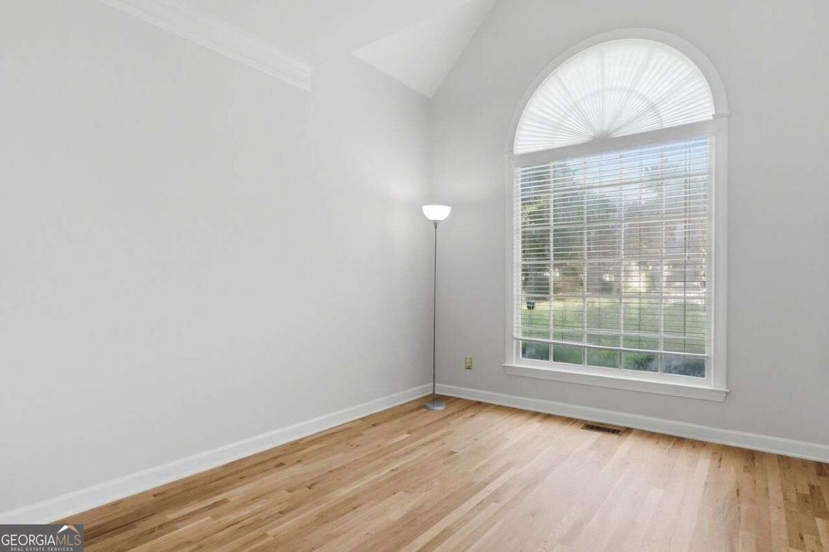 Empty room with light hardwood floors and a large arched window with blinds.