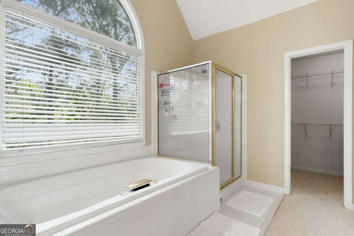 Bathroom with a soaking tub beneath an arched window, glass shower, and open walk-in closet.