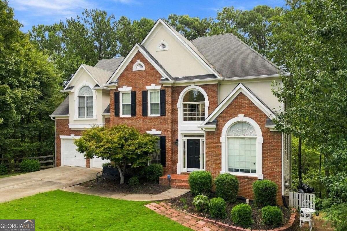 Two-story brick-and-cream home with a gabled roof, attached garage, and mature trees.