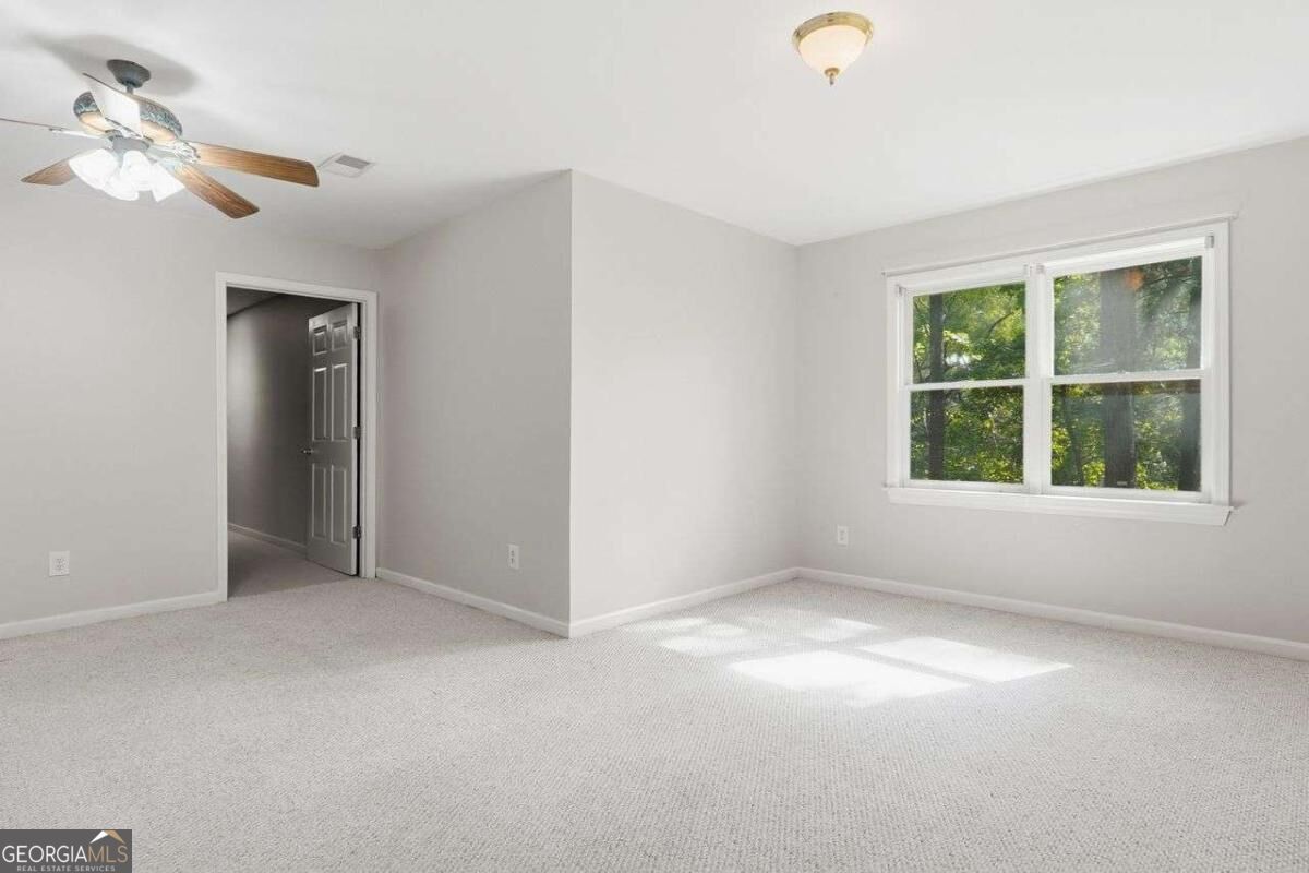 Empty carpeted bedroom with a ceiling fan and a window overlooking trees.