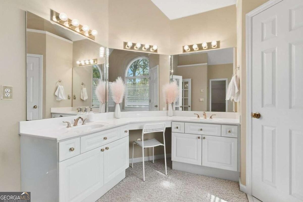 Bathroom vanity with two sinks, a central makeup desk, large mirrors, and an arched window.