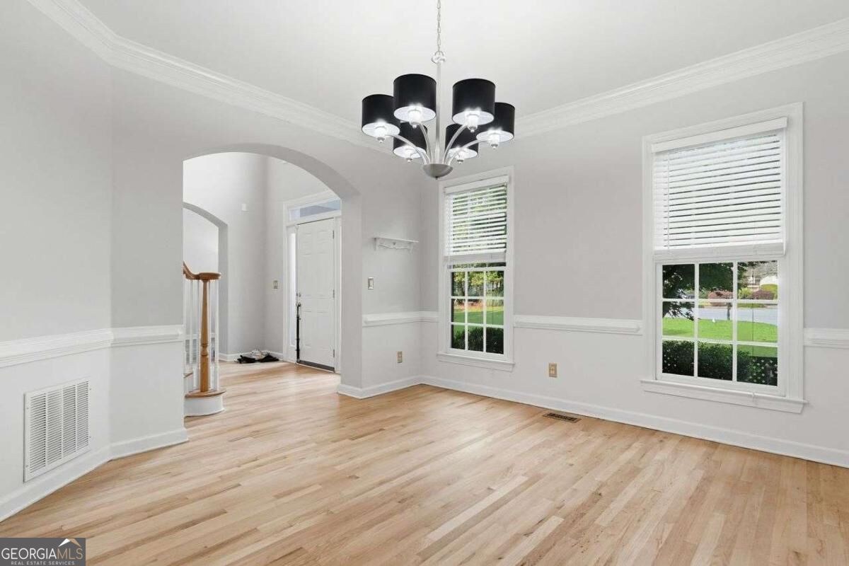 Empty dining room with pale hardwood floors, a black-shaded chandelier, and tall windows overlooking the lawn.