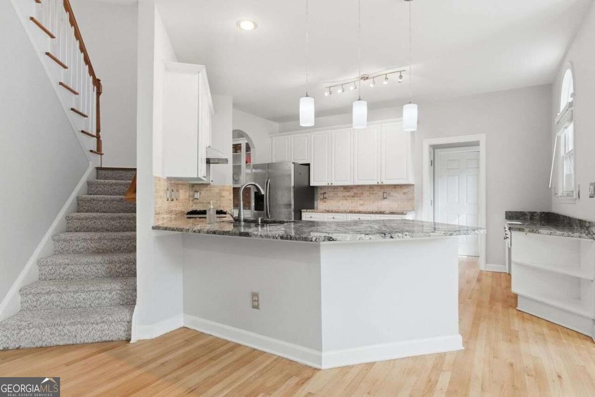 Kitchen with a granite peninsula, white cabinetry, stainless steel appliances, and a carpeted staircase.
