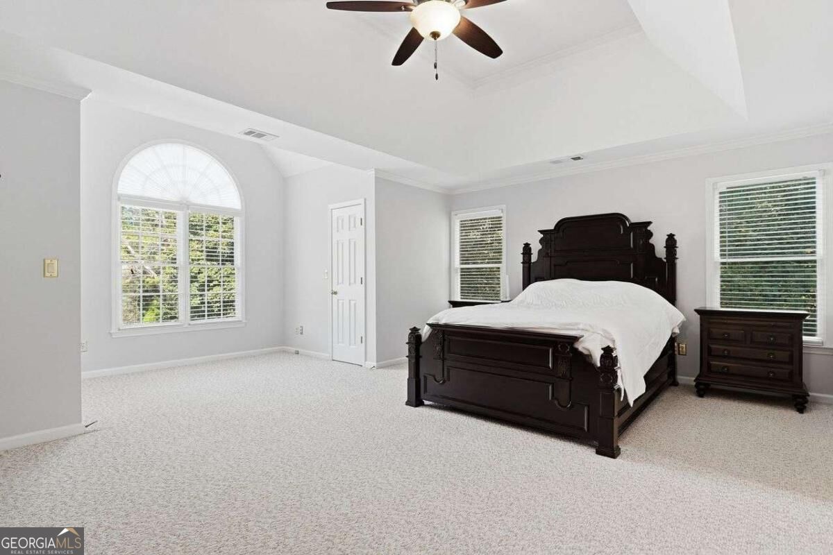 Bedroom with a dark wood bed, arched window, and ceiling fan.