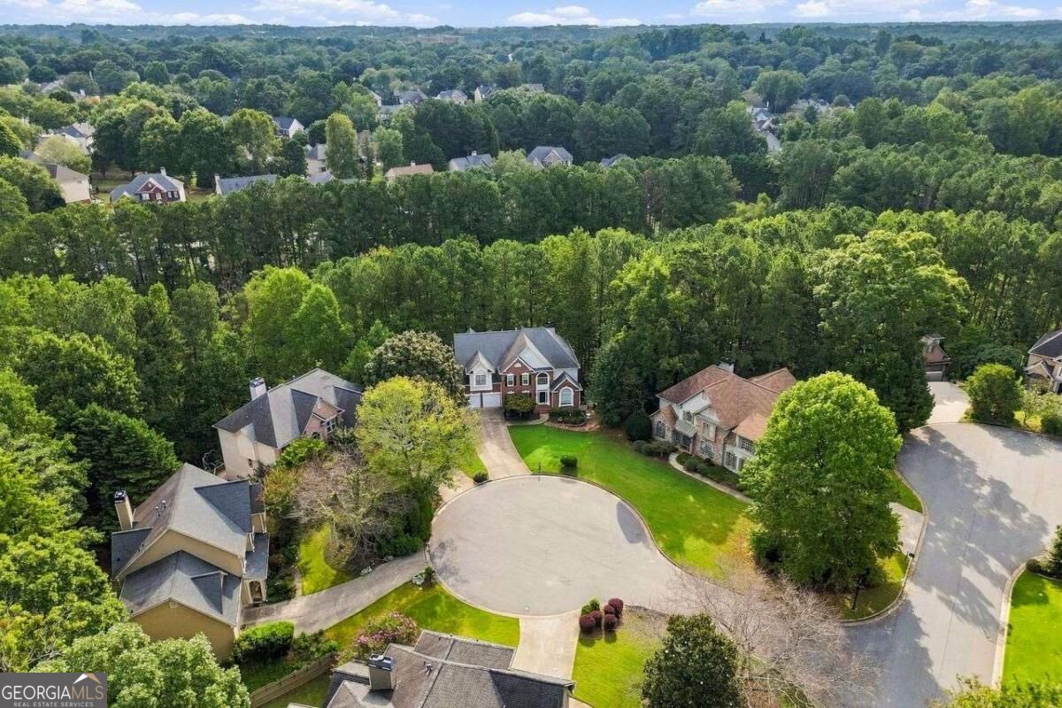 Aerial view of a wooded cul-de-sac with a two-story brick home and neighboring houses.