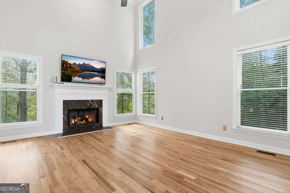 Living room with hardwood floors, tall windows, and a lit fireplace beneath a television.