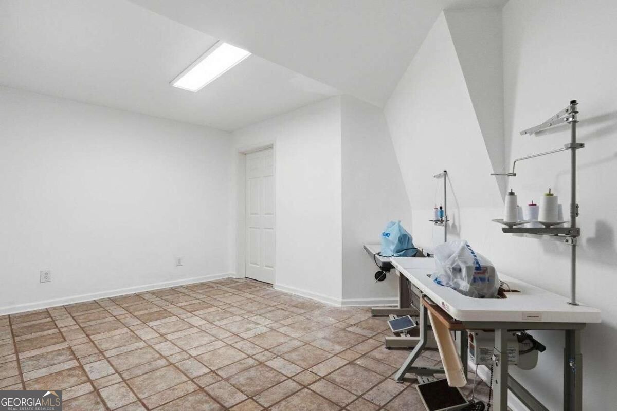 Sewing room with tiled floor, industrial machines, and thread stands along a long worktable.