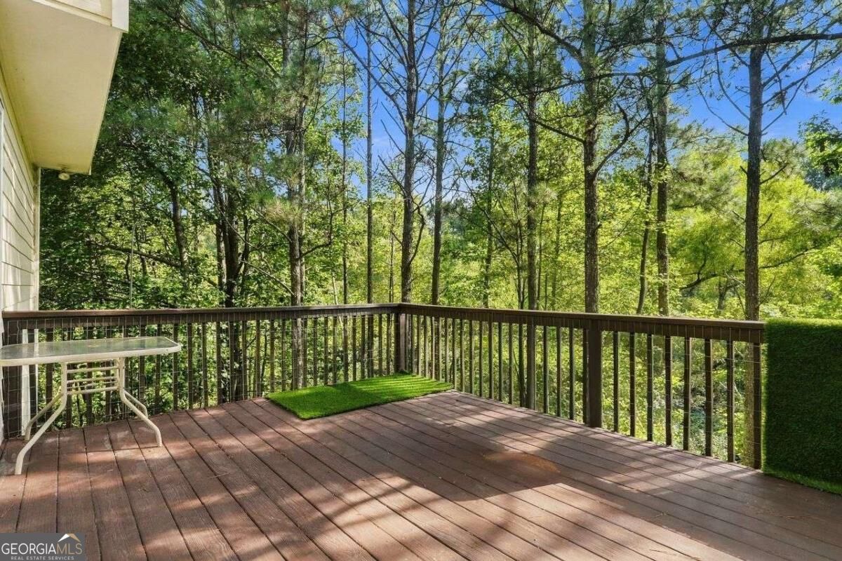 Wooden deck overlooking leafy woods, with a small patio table and a patch of artificial turf.