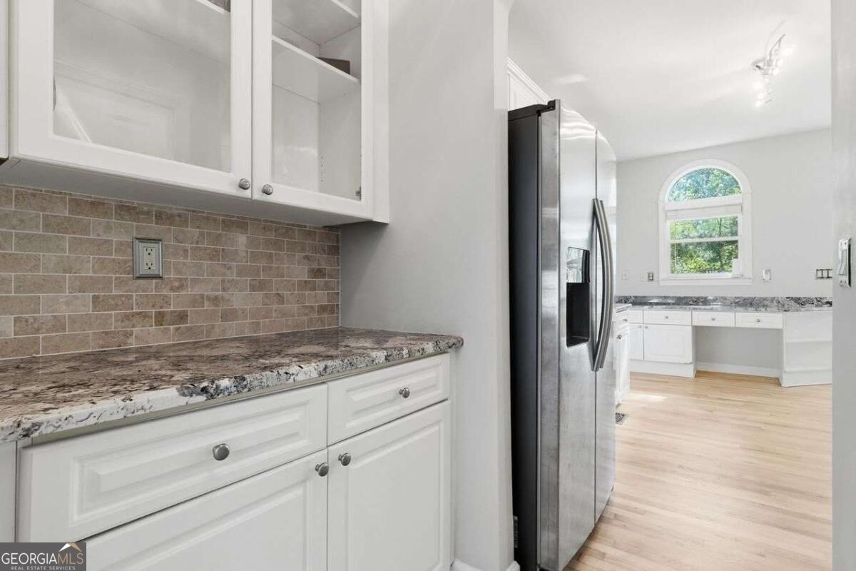 Kitchen with white cabinetry, granite counters, a brick-pattern backsplash, and an arched window.