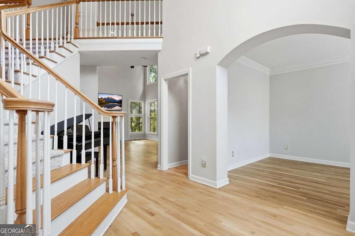 Two-story foyer with a wood staircase, white railings, black piano, and wide arched opening.