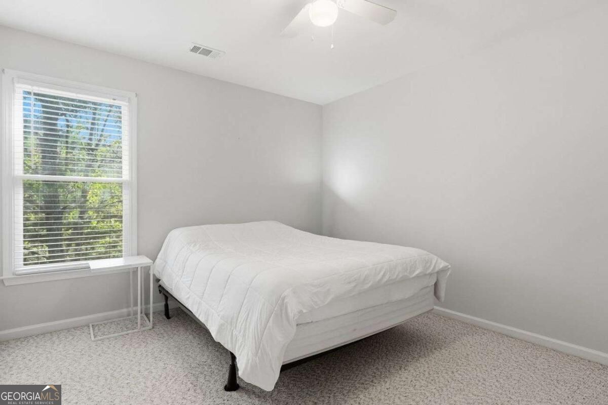 Bedroom with a white bed, beige carpet, and a window overlooking green trees.