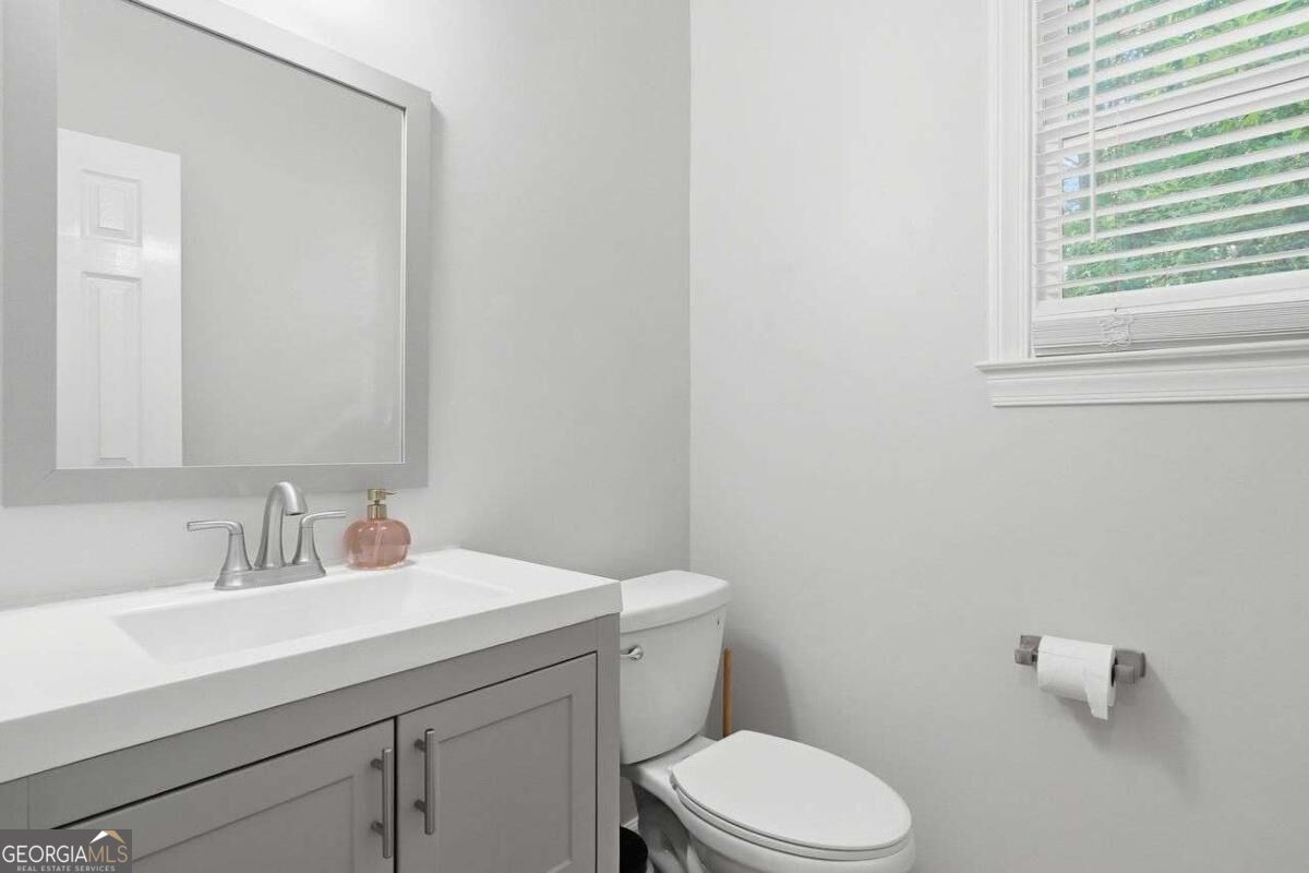 Bathroom with gray vanity and framed mirror beside a toilet and window with white blinds.