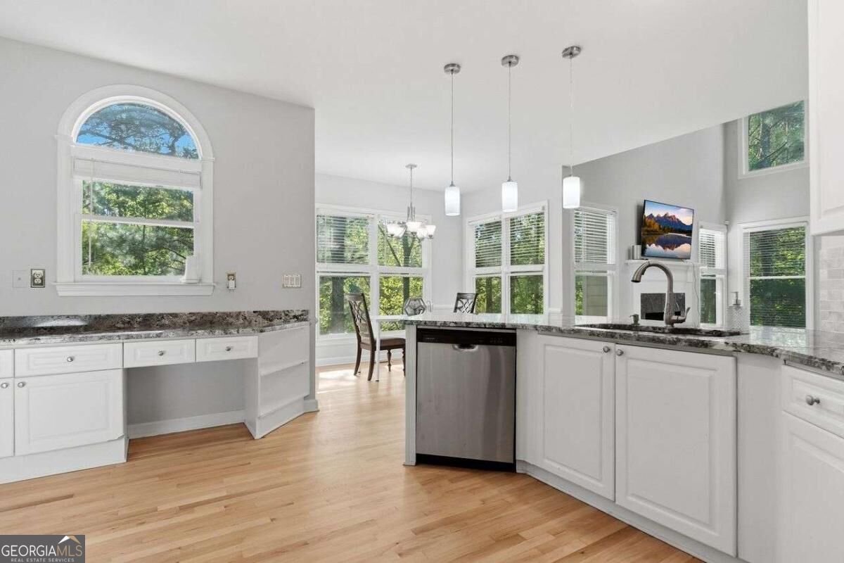 Bright white kitchen with granite counters, hardwood floors, and large windows overlooking trees.