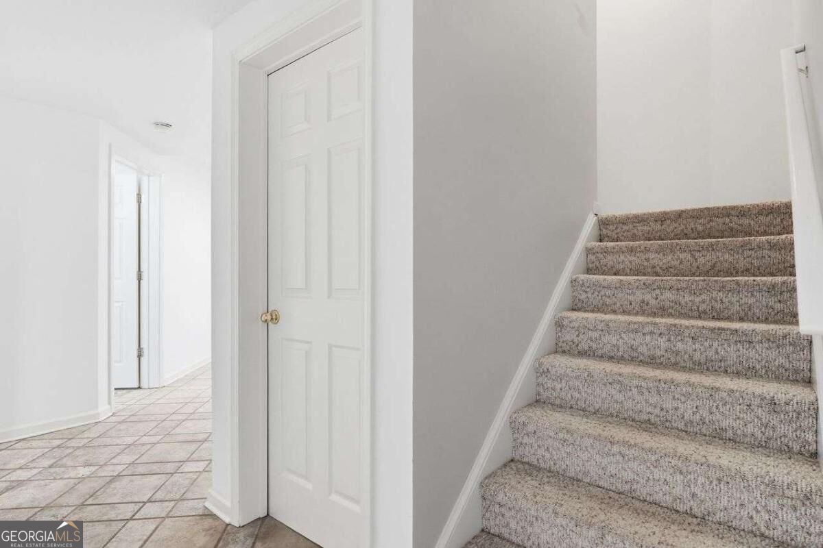 Vacant hallway with a carpeted staircase beside a tiled corridor and white paneled doors.