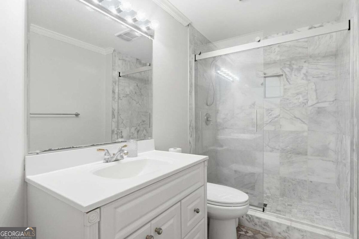 Bathroom with a white vanity and sink beside a marble-tiled glass shower.