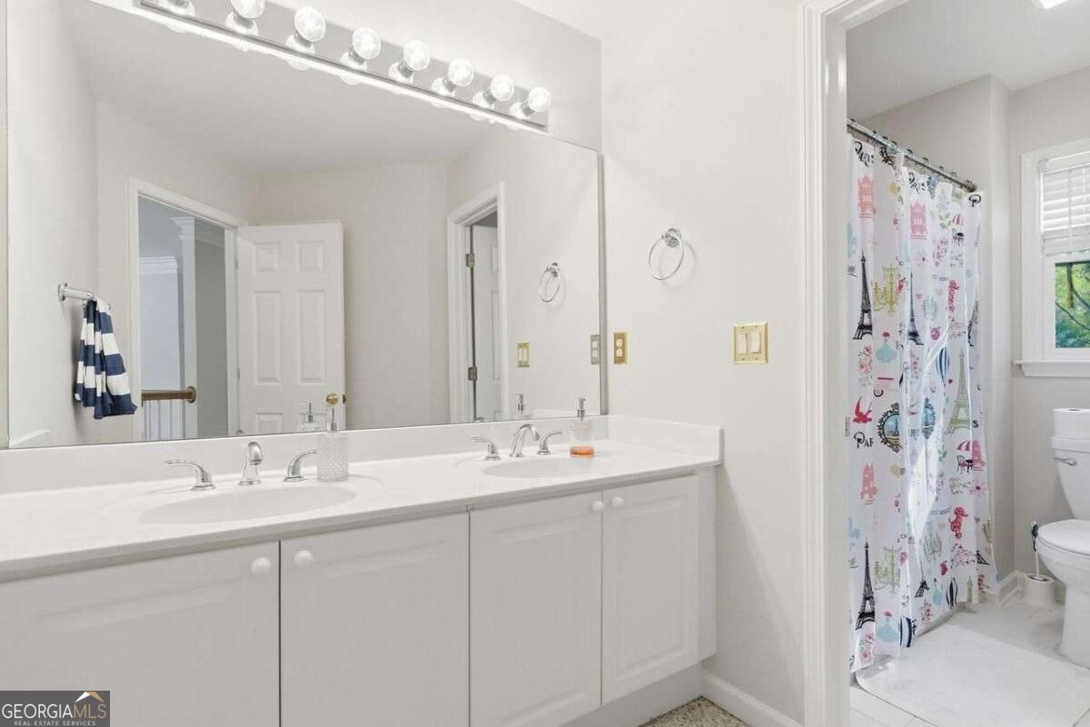 Bathroom with a long double-sink vanity, broad mirror, and colorful shower curtain.