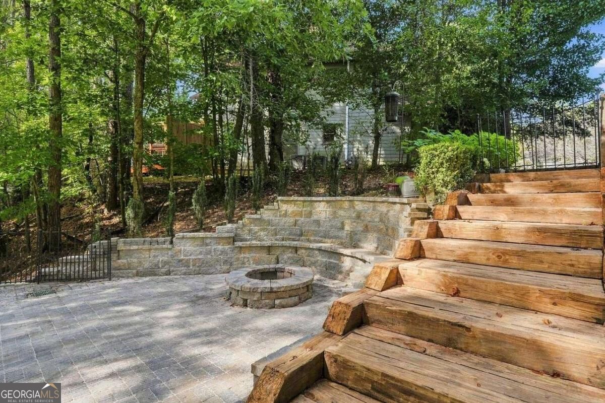 Wooded backyard patio with a circular stone fire pit and broad timber steps.