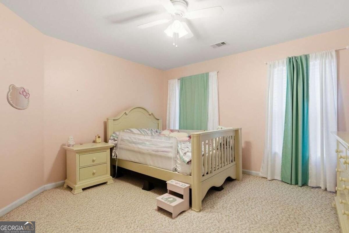Bedroom with a light-colored toddler bed, peach-pink walls, and green-and-white curtains.