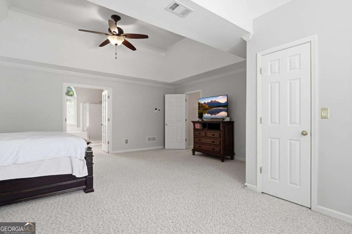 Furnished bedroom with a dark wood bed, carpeted floor, and ceiling fan beneath a stepped ceiling.