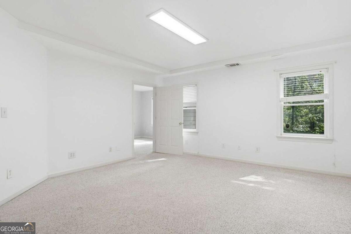 Empty carpeted room with white walls, two windows, and an open doorway.