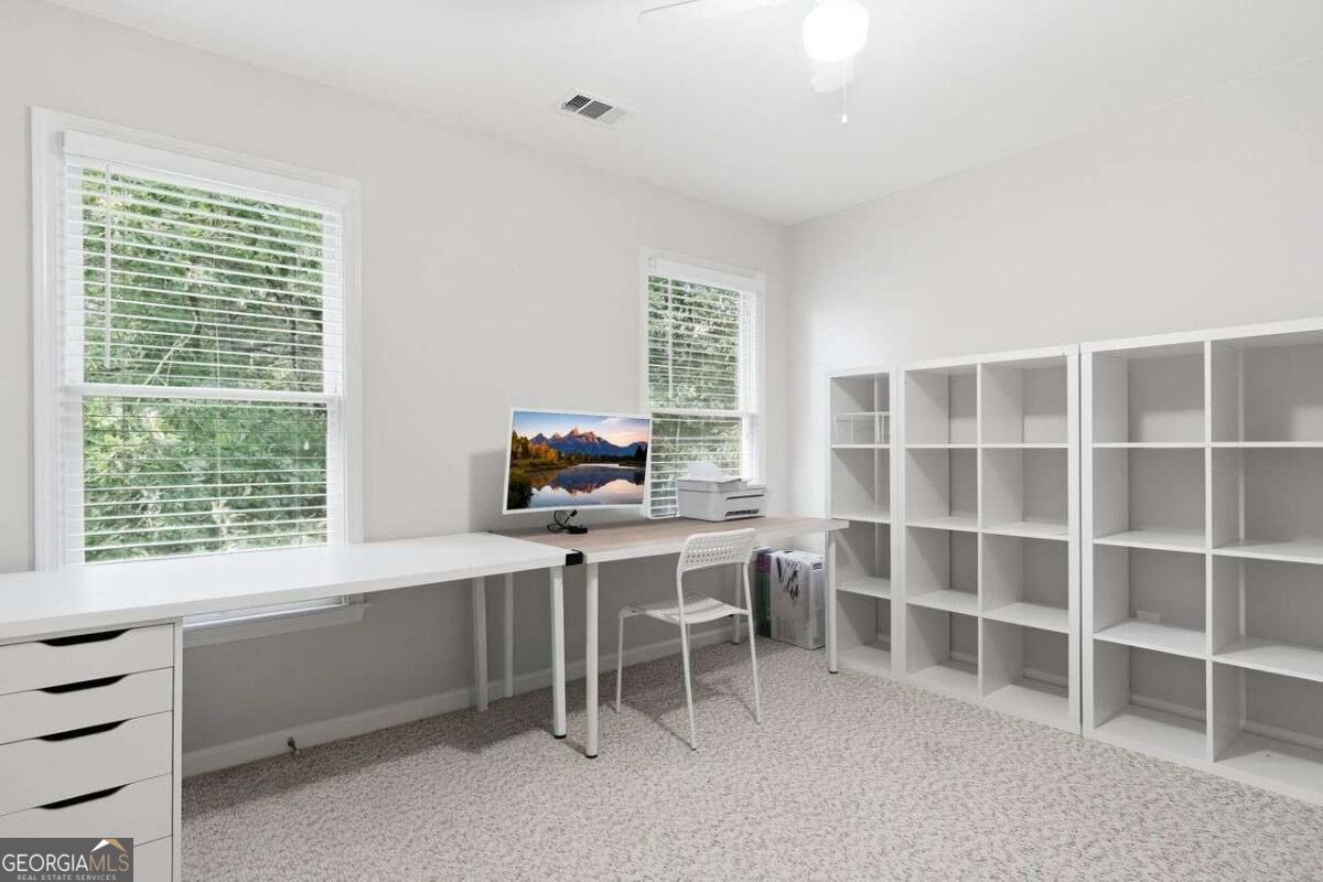 Home office with white desks, built-in shelving, and two windows overlooking greenery.