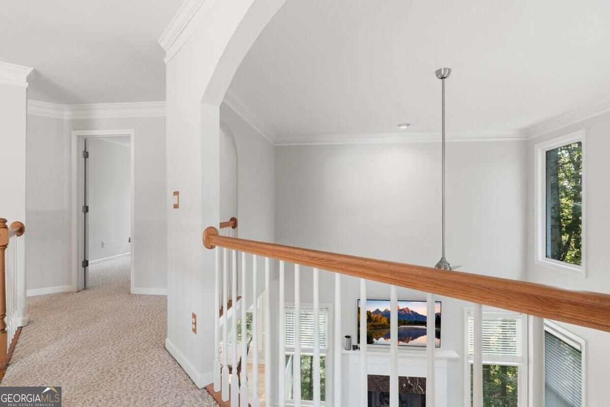 Upstairs landing with beige carpet and wood railing overlooking a bright living room with a fireplace.