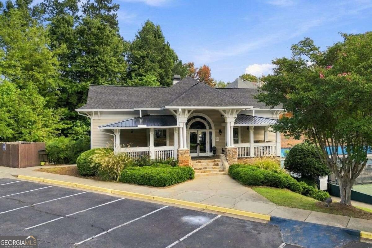 Building with white-columned porches, an arched entrance, stone steps, and landscaped shrubs beside a parking lot.
