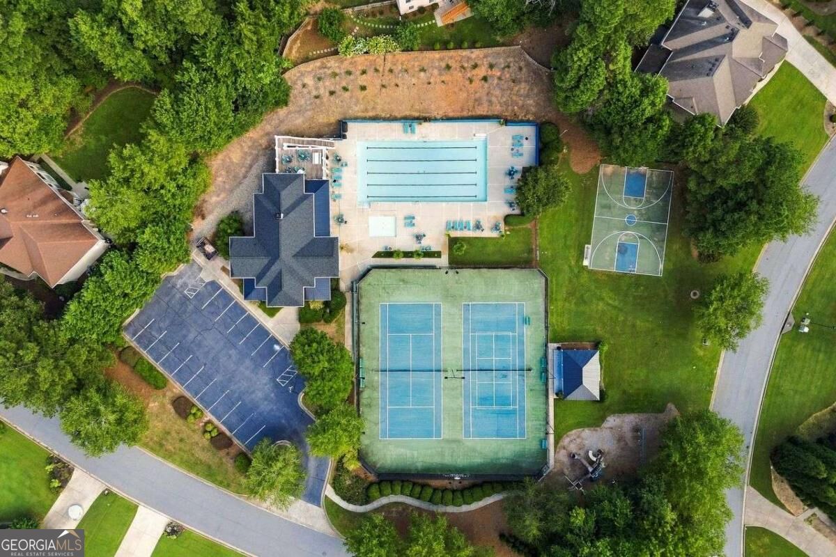 Aerial view of a swimming pool, tennis courts, and basketball court amid trees.