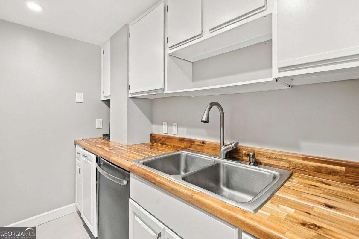 Kitchen with butcher-block counters, white cabinets, and a double-basin stainless steel sink.