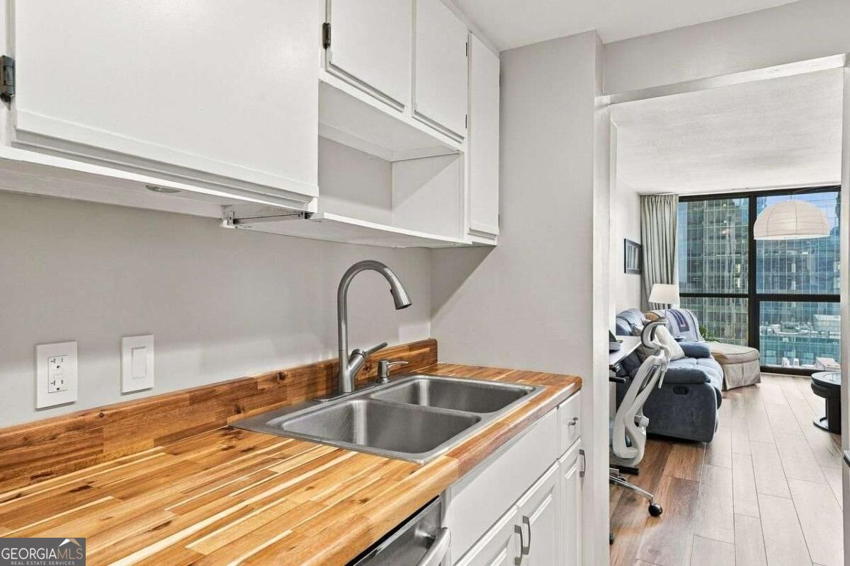 Apartment kitchen with butcher-block counters and double sink, opening onto a furnished living room with city views.