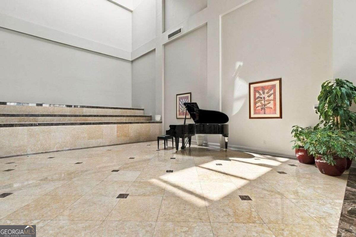 Double-height lobby with a grand piano, stone-tile floor, and potted plants.