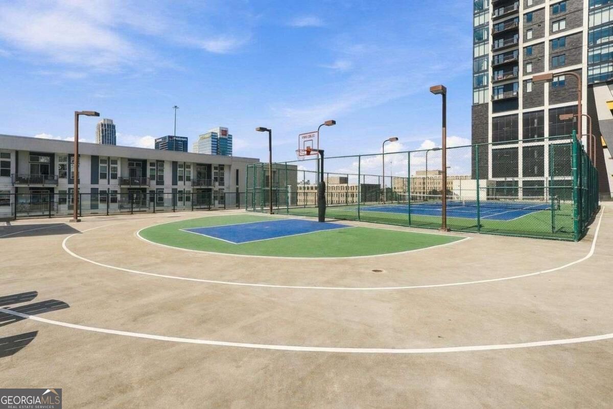 Outdoor basketball court beside a residential tower, with downtown buildings in the distance.