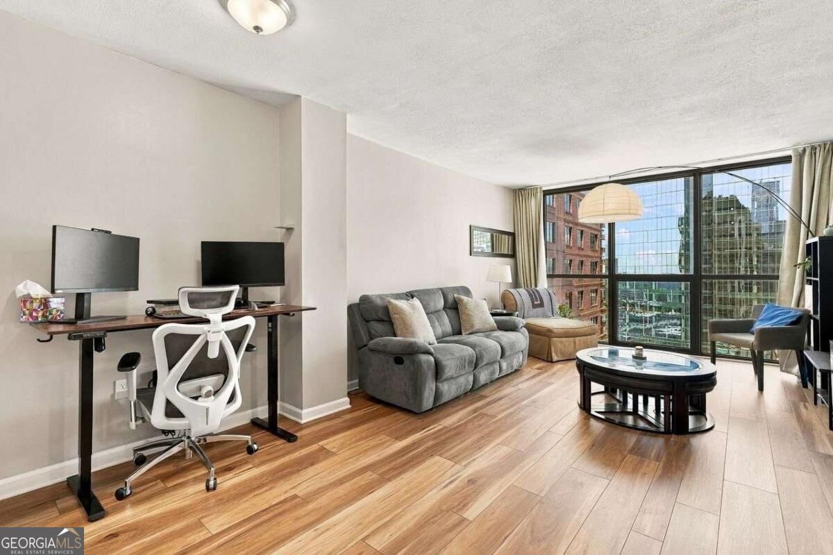 Condo living room with a desk and dual monitors beside large windows overlooking the city.