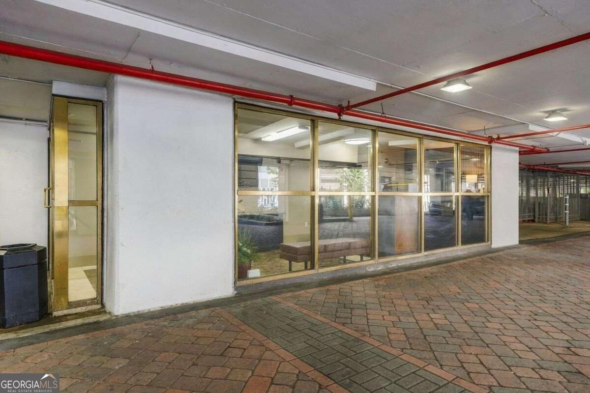 Glass-fronted building entrance with brass-framed doors beside a brick-paved walkway.