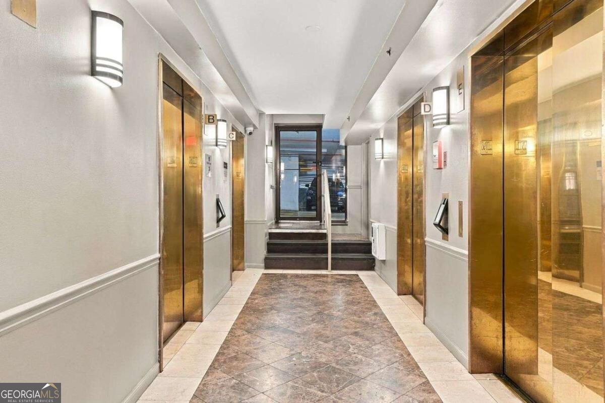 Elevator lobby with brass doors, marble flooring, and steps to a glass entrance.