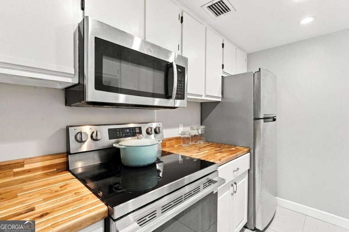 Kitchen with butcher-block counters, white cabinets, and stainless steel appliances.