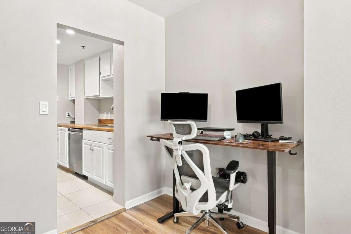 Home office with a wood-top desk, dual monitors, ergonomic chair, and adjacent kitchen.