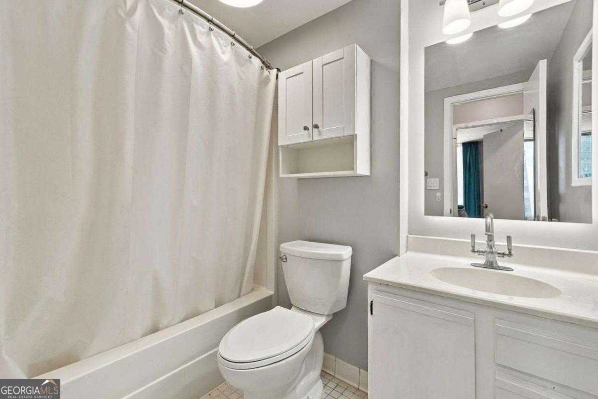 Bathroom with a white tub and shower curtain, toilet, and vanity beneath a large mirror.