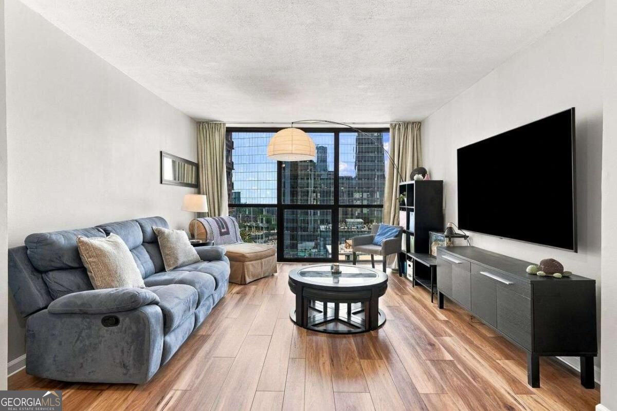 Condo living room with a blue sectional and floor-to-ceiling windows overlooking city buildings.