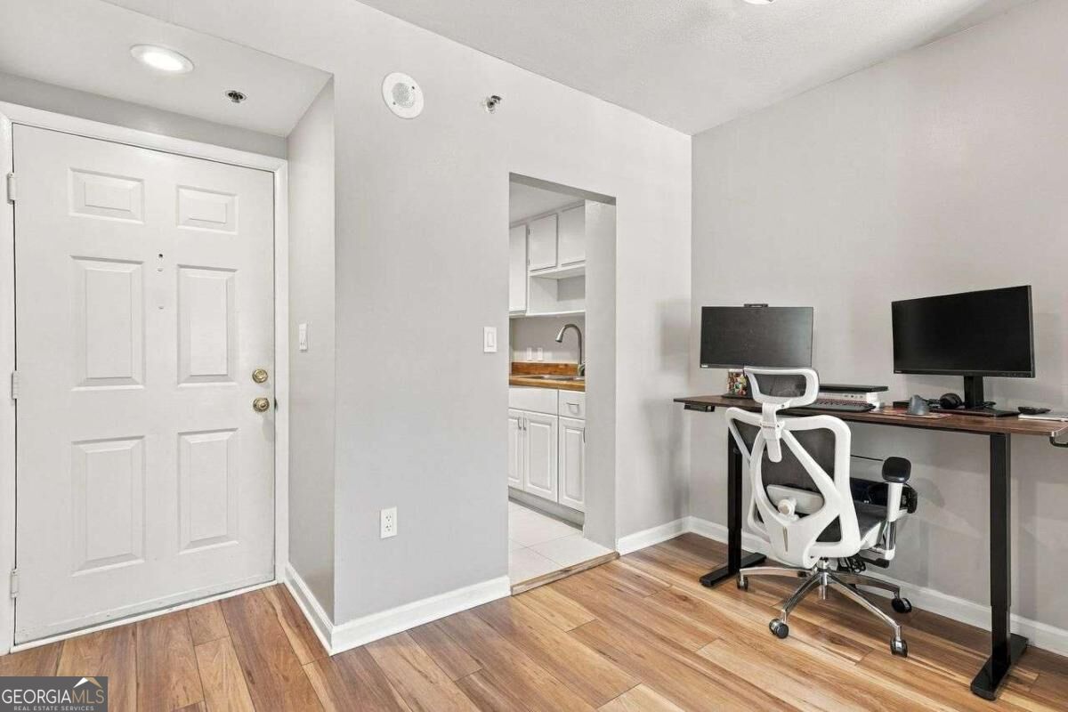 Condo entry and office with wood flooring, a white front door, and a desk with two monitors.