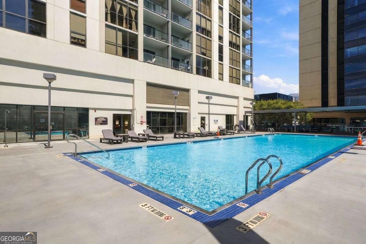 Outdoor swimming pool beside a modern high-rise condominium, with deck loungers.