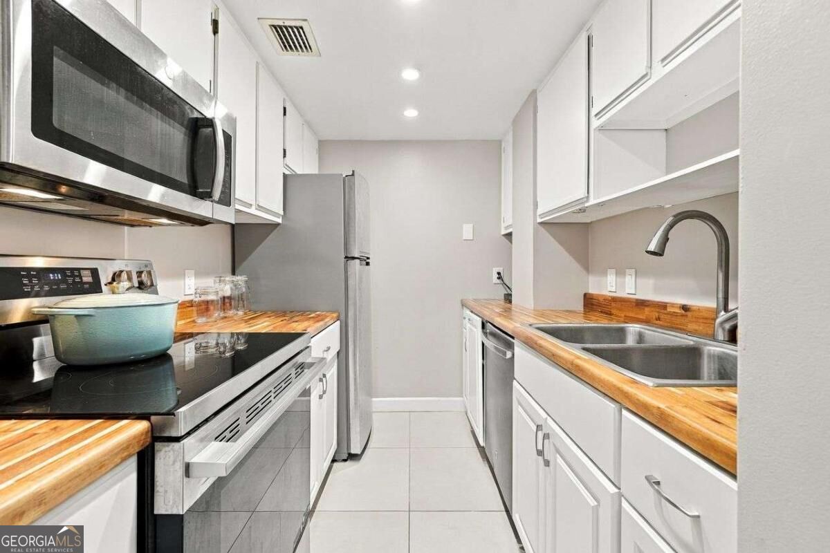 Narrow kitchen with stainless appliances, white cabinets, butcher-block counters, and a double-basin sink.